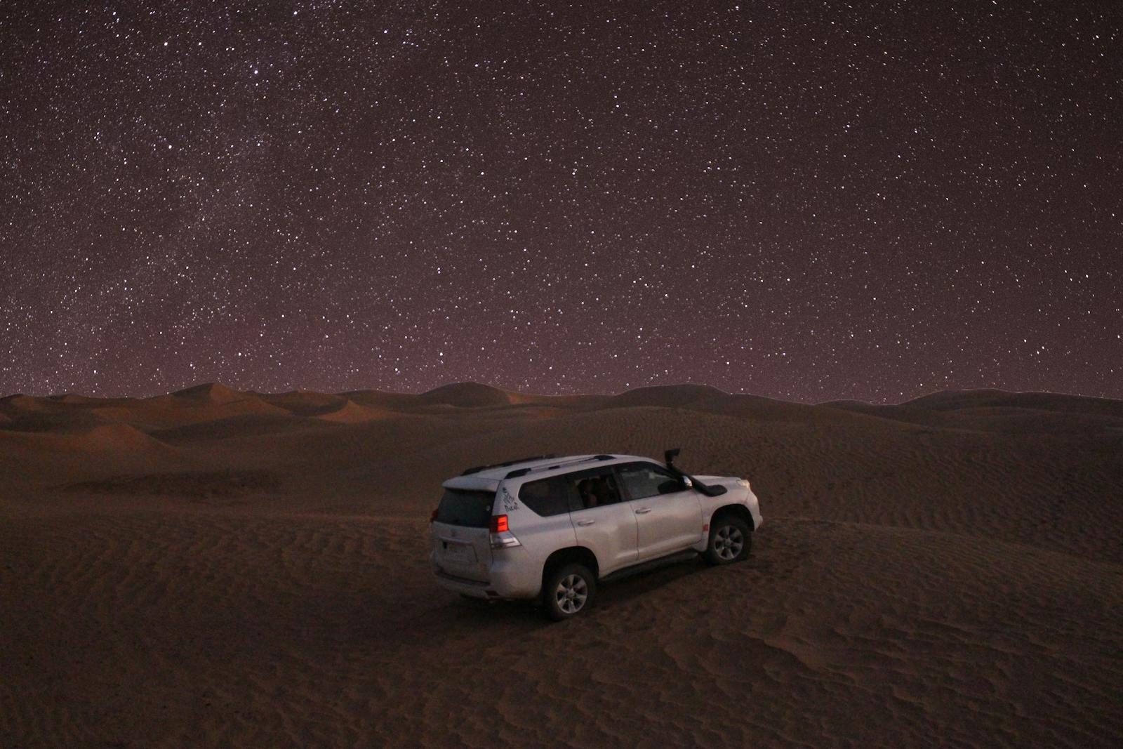 A lone car under a starry sky in the picturesque Merzouga sand dunes.